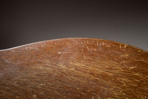 A close-up on Woody Guthrie's guitar shows the phrase, "This machine kills fascists" scratched into the wood.