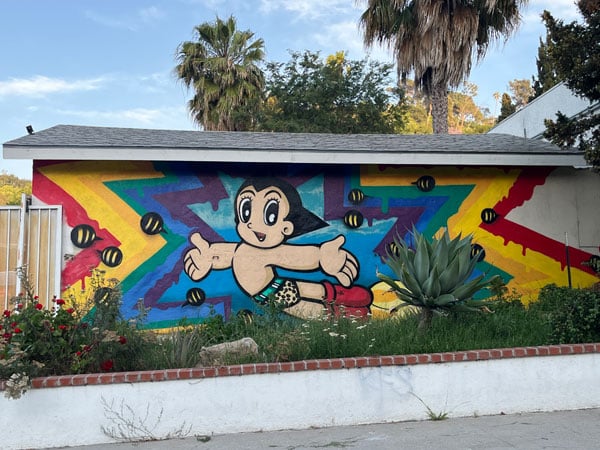 A colorful mural on the side of a building show the character of Astro Boy surrounded by a rainbow starburst.