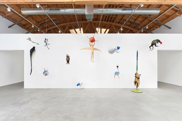 An installation view of a gallery shows several sculptures of otherworldly creatures dangling from the ceiling.