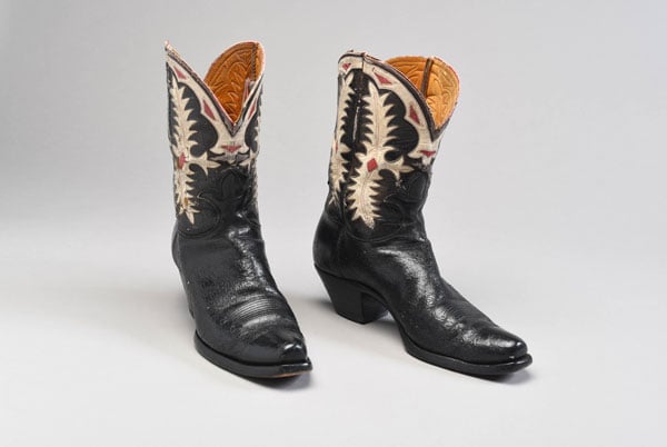 A bair of vintage black cowboy boots feature eleborate patterns on in white on red on the sides.