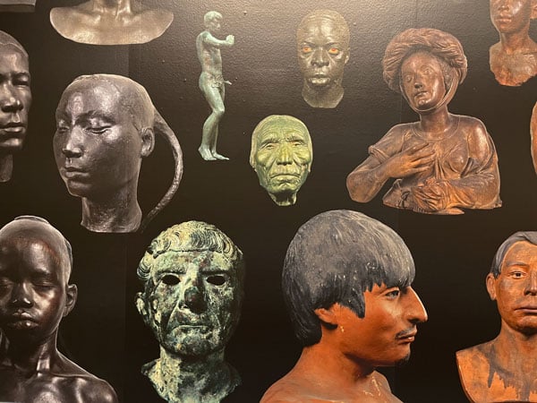 A detail of an art work by Ken Gonzalez-Day shows a black wall vinyl with different images of sculptures of human faces of different races arranged in a pattern.