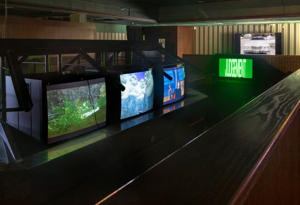 A row of television sets playing video art rest on a salad bar structure at a defunct Sizzler.