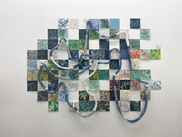 An elaborate multimedia collage by Fran Siegel mixes images of differen plant species on different colored tiles, which are connected by a looping "vine" made out of rope.