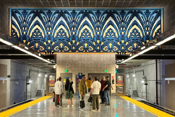A mural by Mark Dean Veca featuring stylized Gothic arches rendered in sparkling blue stands above a metro station on LA's D line