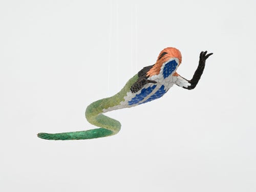 A piñata in the form of a hybrid lizard/snake dangles from a gallery ceiling.