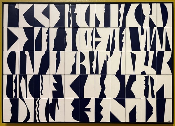 A multimedia work by Howard Smith features a wall panel made out of white tiles covered in black forms and glyphs.