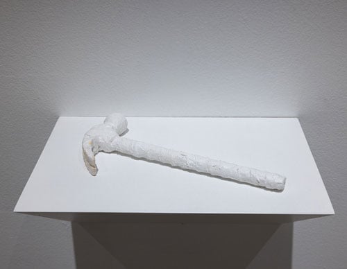 A hammer wrapped in which bandages rests on a white shelf — a sculpture by Jamison Carter