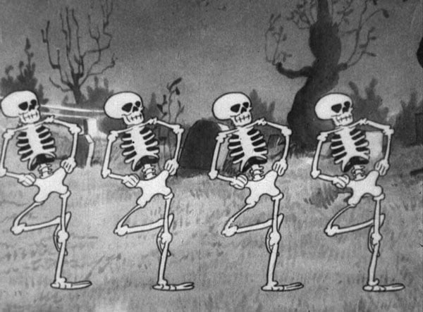 A still from a vintage black and white cartoon shows a row of four skeletons dancing.