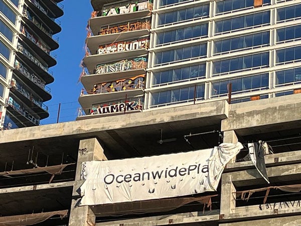 An incomplete tower covered in graffiti features a tarp that reads "Oceanwide Plaza."
