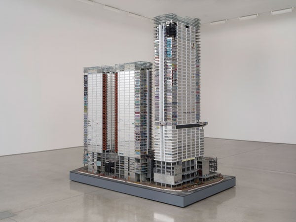 A sculpture built to resemble the Oceanwide Plaza mega development stands in a white walled gallery.