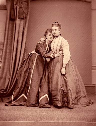 A sepia photo shows the Victorian-era duo Fanny and Stella — male theater performers wearing Victorian gowns — in an embrace.