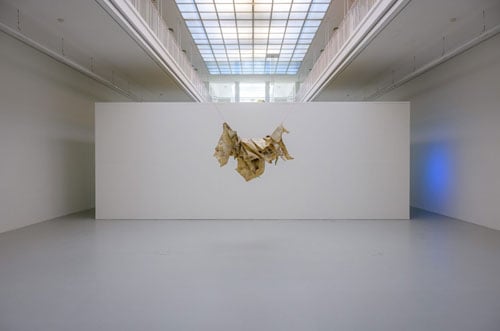 A sculpture made from rawhide hangs from a ceiling, resembling a flapping bird.