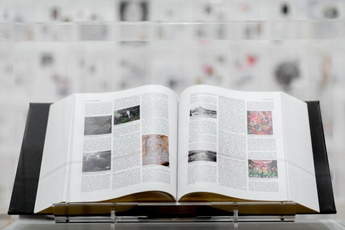 An encyclopedia-like book is displayed in a gallery with walls covered in encyclopedia-style pages.