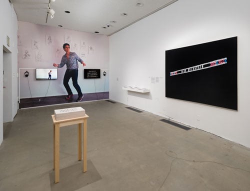 An installation view of an exhibition shows a large wall vinyl of a woman dancing.