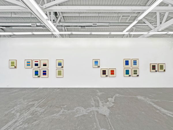 A view of a gallery wall shows a series of framed works made up of bright bands of color.