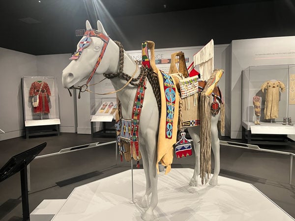 A museum installation shows a dummy of a horse draped with a beaded saddle and other decorative elements.
