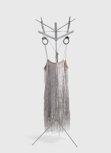 A sculpture shows a sparkling silver dress attached to a music stand with handcuffs