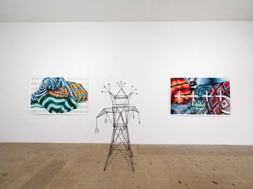 Two paintings of Navajo blankets by Nani Chacon hang behind a small sculpture that resembles an electrical tower crafted in the form of a deity.