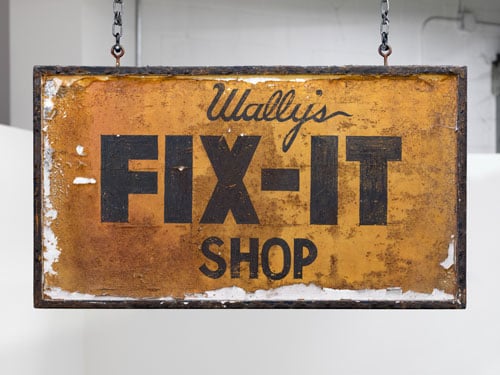 An old sign hanging from a ceiling reads, "Wally's Fix-It Shop."