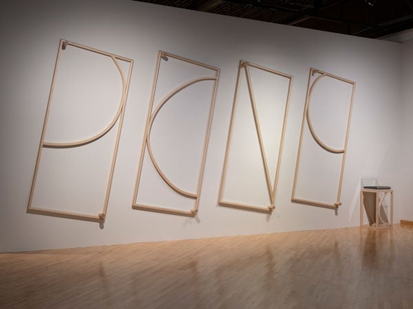 A series of four wooden sculptures on a wall show various shapes — like a line and a semi circle — framed by thin bands of wood.