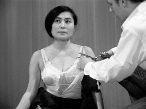 A black andwhite still shows a man cutting Yoko Ono's camisole straps as part of her performance "Cut Piece."
