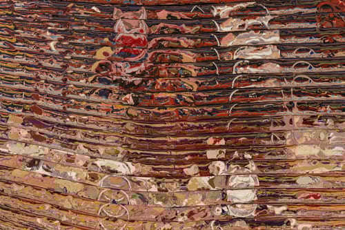 A close-up of a canvas shows layers of paint in brown, pink and white spread in ripples across a canvas.