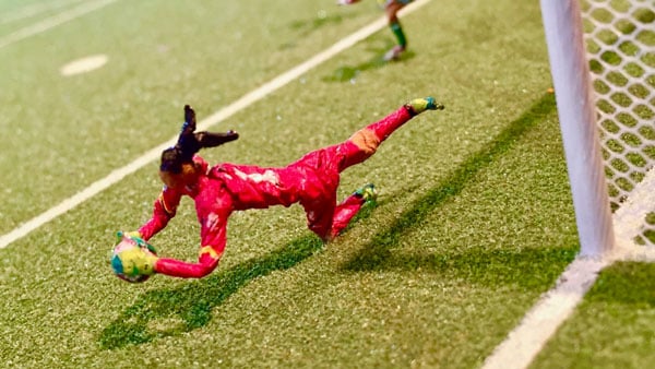 A still from a stop motion animated artwork by Lyndon Barrois, Sr. shows a female soccer goalie in a red uniform halting the advance of a ball by throwing her body on the ground.