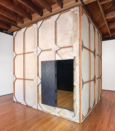In a gallery stands a larger-than-life cube made out of stretched, painted canvases that are all black inside.