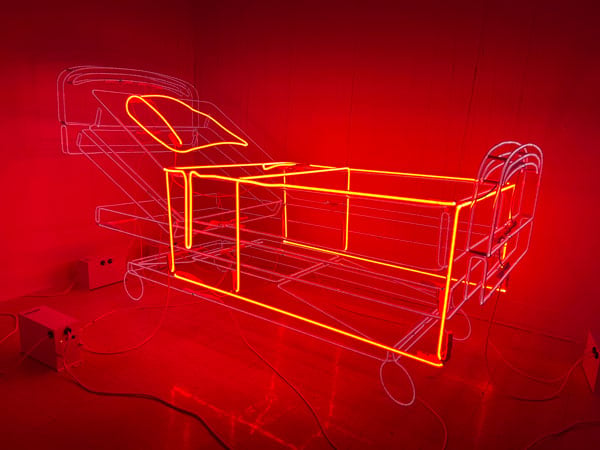 In a room sits a hospital med made entirely out of red neon light.