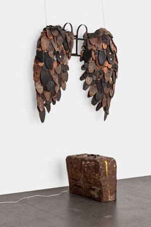 A sculpture appears to show an old briefcase and a set of wearable wings. The wings are fabricated out of the soles of old shoes.