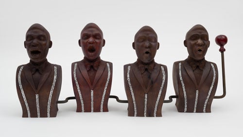 A sculpture shows the busts of four Black men, all with open mouths as if singing. They wer suits with silver stripes.