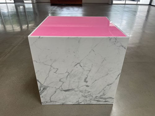 A sculpture by Charles Ray consists of a marble plinth featuring a think pool of bright pink Pepto-Bismol on top.