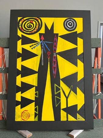 A large, bright painting, featuring an abstracted figure at center surrounded by a black and yellow triangular pattern, rests on supports in a conservation lab.