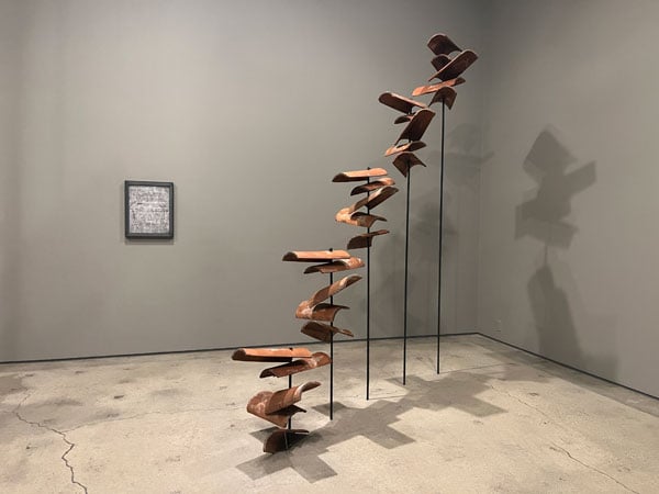 An installation by Jackie Castillo in a gallery shows a series of terracotta roof tiles threaded through pieces of steel —&nbsp;looking as if they are falling from the sky.