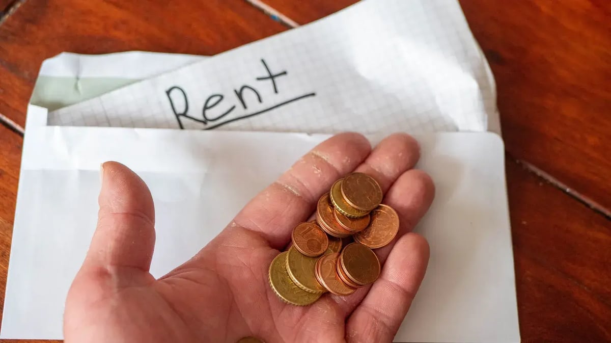 A person holds coins with a rent envelope in the background