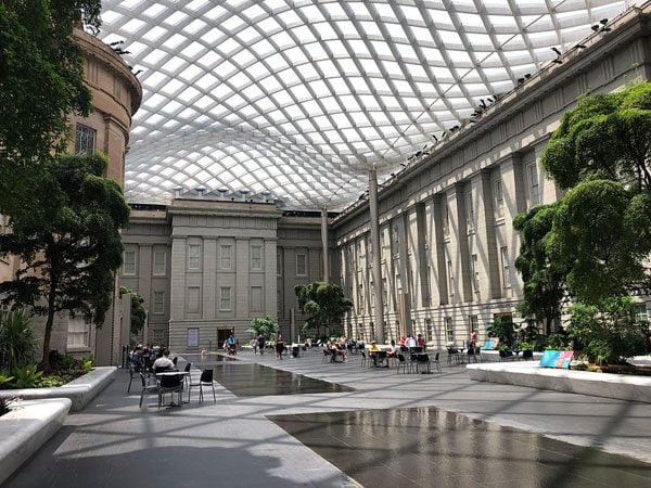 A brightly lit courtyard in a museum is topped by undulating glass in a geometric pattern