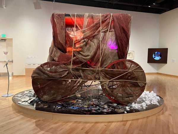 A sculpture of a jesup wagon is shrouded in burlap and othe rmaterials