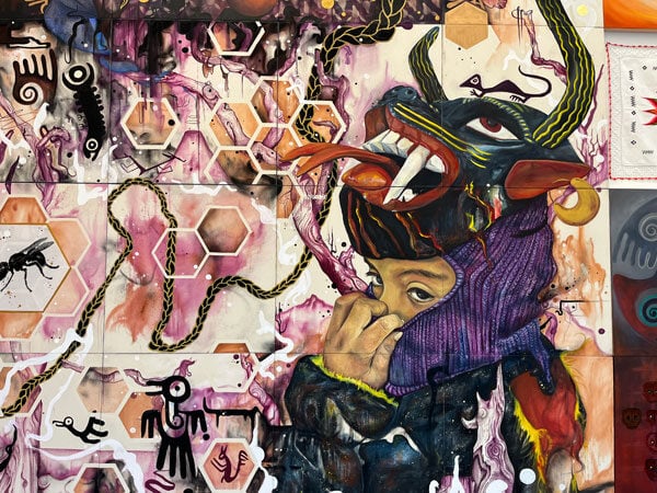 A detail of a brightly colored mural shows a young person wearing a folkloric devil mask