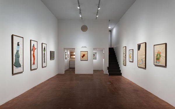 A horizontal image shows a gallery space hung with paintings that incorporate ravens