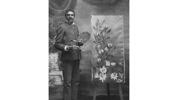 A Black man stands before an easel with a painting of a flower in a vintage black and white photo