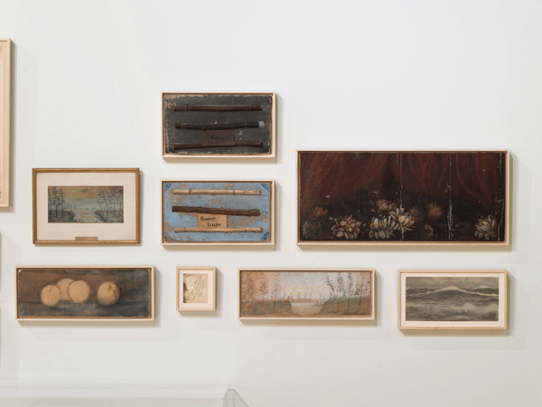 A cluster of small nature paintings hang in a gallery