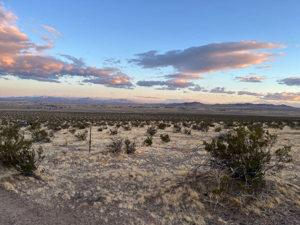 A view of a desert hillside at dusk. Clouds reflecting the sunlight hover over the horizon.