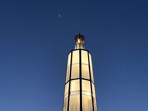 The top of a ligthhouse is seen against a blue sky at dusk.