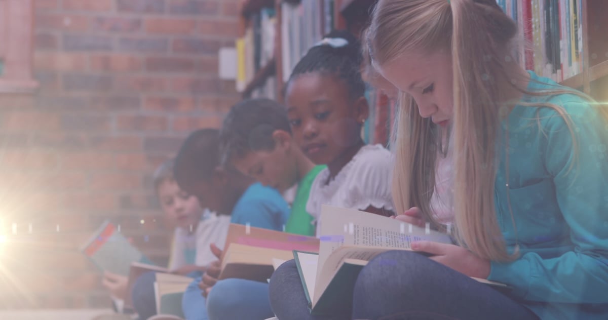 Image of light trail over diverse schoolchildren reading books in library. childrens book day and celebration concept digitally generated image - via Shutterstock-1