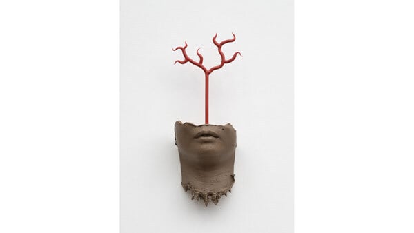 A sculpture by Kelly Akashi shows part of a human face with a branch growing out of it.