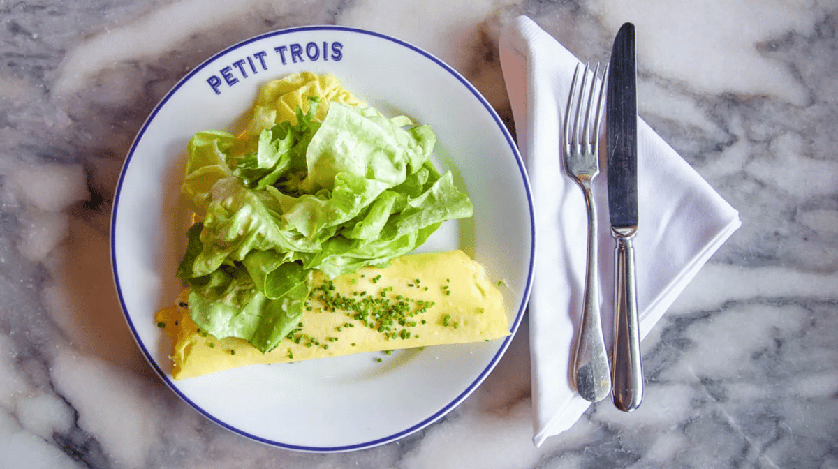 The omelet at Petit Trois, made with three eggs, butter, salt, white pepper, Boursin, and chives, is served with a simple side salad. Photo by Capra Photography.