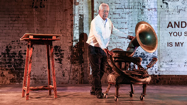 Artist William Kentridge appears on a stage next to a large tuba