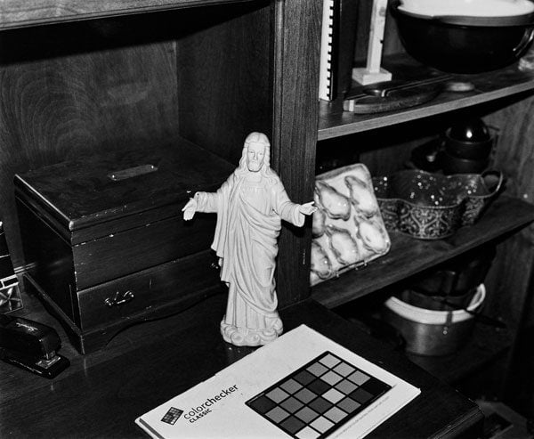A black and white picture shows a porcelain sculpture of Jesus with a broken hand