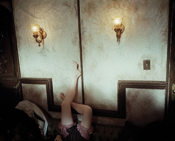 A color photograph by Yorgos Lanthimos shows a woman's legs running up a wall with 19th century sconces
