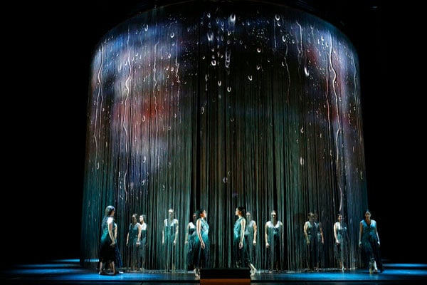Performers weave in and out of a translucent curtain made of fringe on a stage
